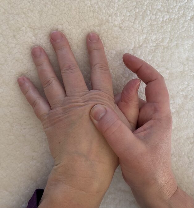 Photo of two hands together with the thumb of one hand massaging below the knuckle of the second hand. 