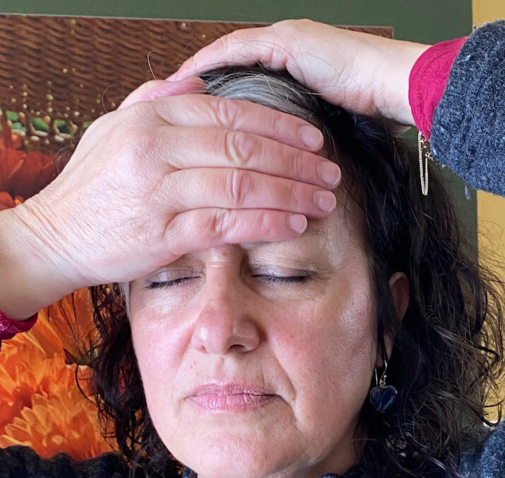 Face view of woman's head with one hand covering her forehead and the other hand covering the top of her head .
